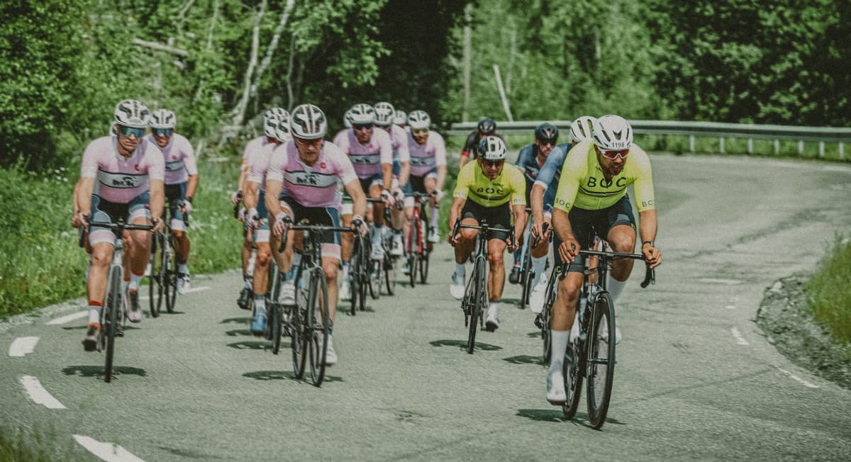 BOC-ryttere i gul klubbdrakt sykler i en samlet gruppe sammen med ryttere i rosa drakter på en skogsvei under Styrkeprøven 2023