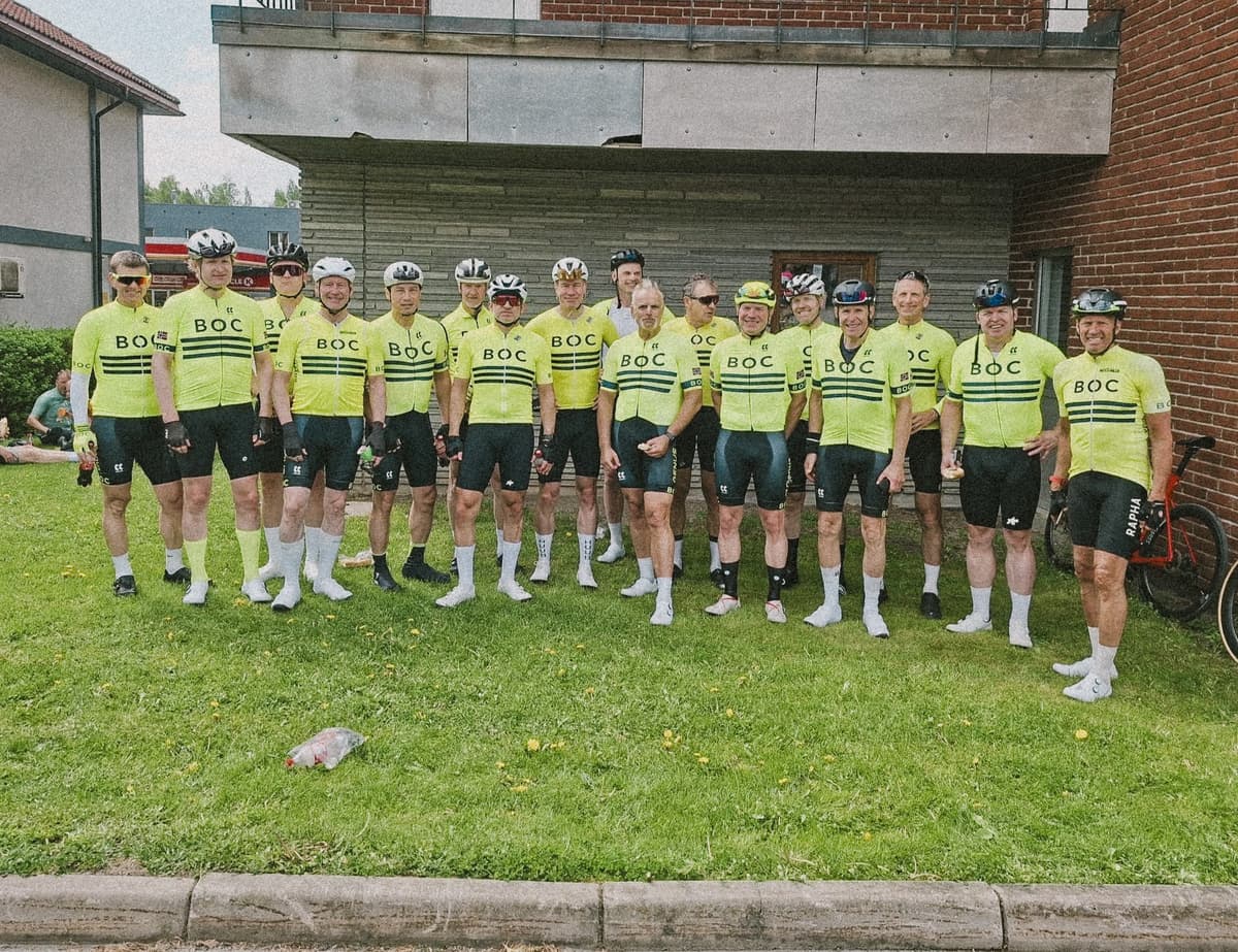 Rundt tjue ryttere i gul BOC-drakt stiller opp på plenen foran et murbygg