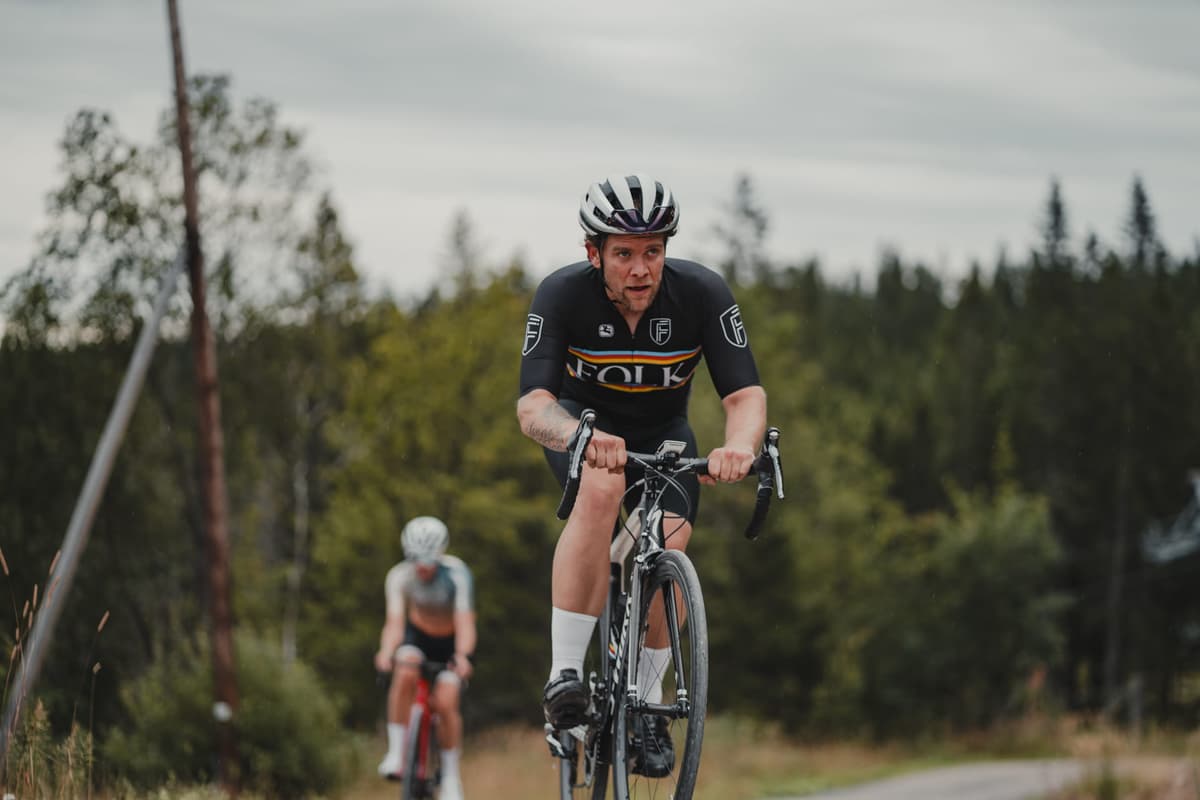 Syklist i svart drakt kommer mot kameraet på en grusvei, med en rytter bak