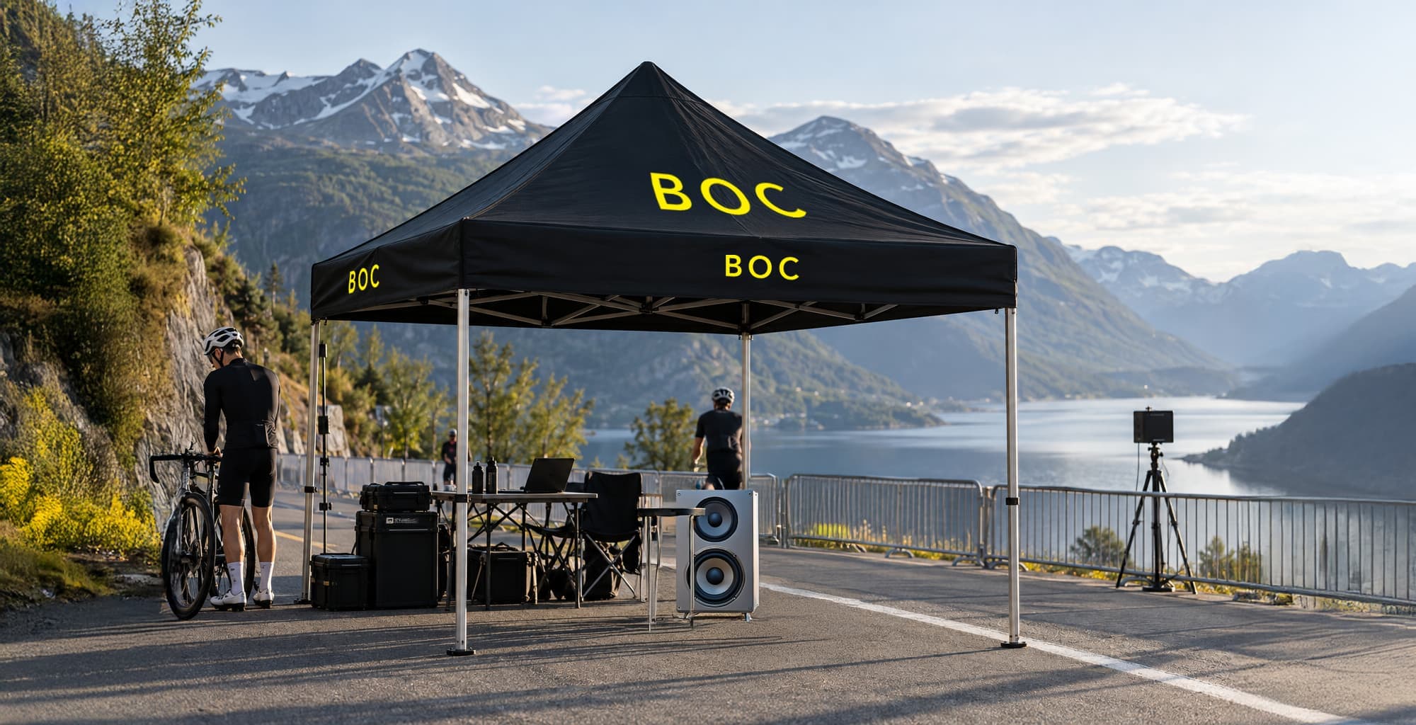 Svart teltoverbygg med gult BOC-ordmerke ved en fjordvei